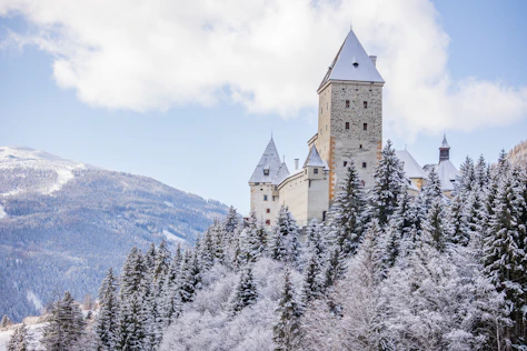 Majestätische Burganlage auf einem verschneiten Hügel mit Blick auf die umliegende Berglandschaft – eindrucksvoll, ruhig und von zeitloser Schönheit.