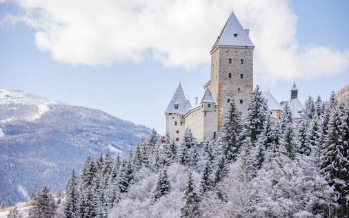 Majestätische Burganlage auf einem verschneiten Hügel mit Blick auf die umliegende Berglandschaft – eindrucksvoll, ruhig und von zeitloser Schönheit.