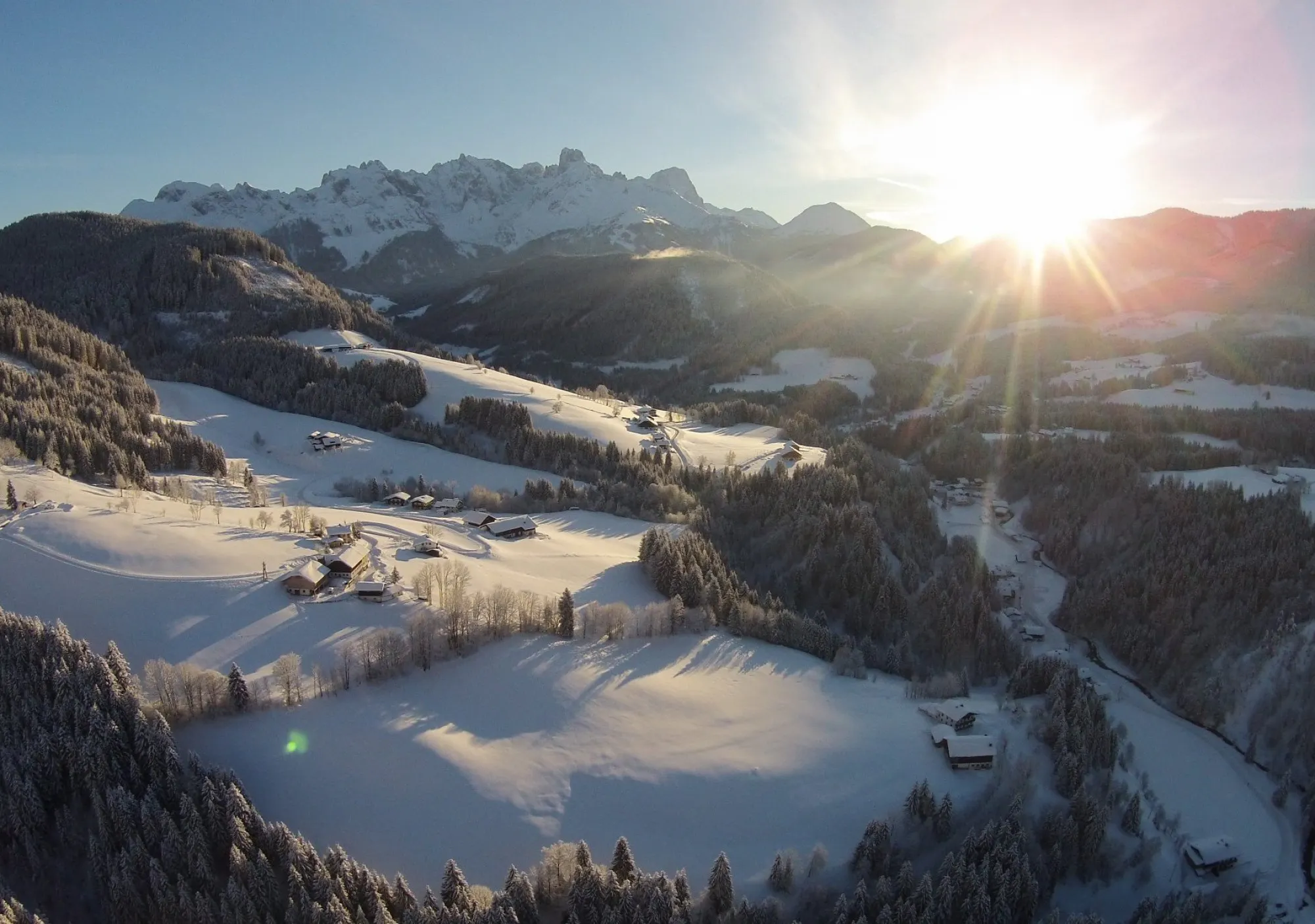 A winter mountain lake surrounded by snow-covered slopes, bathed in the warm light of the low sun—calm, clear, and impressive.