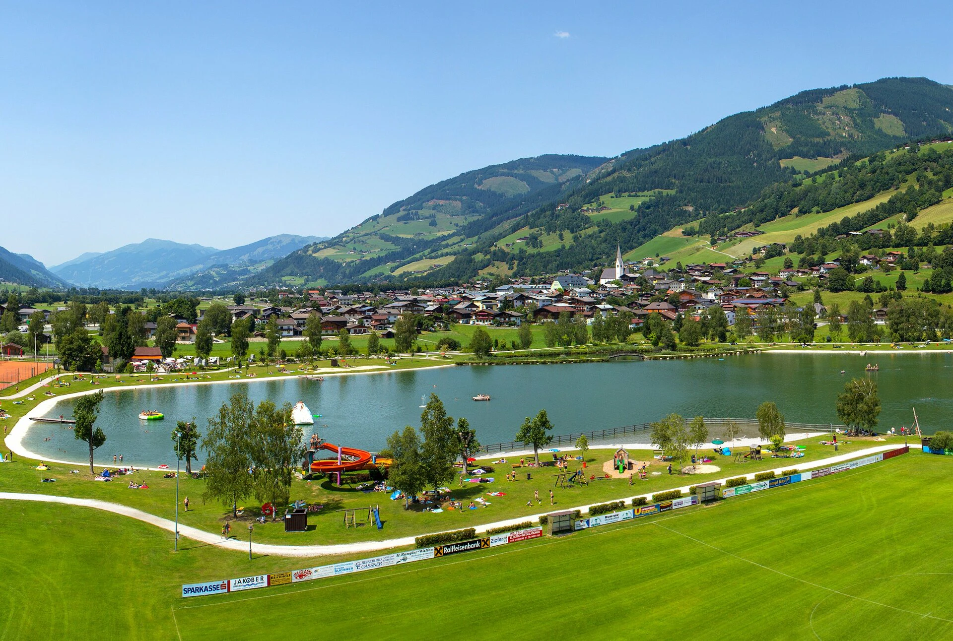 An idyllic lake nestled in a green landscape with views of gentle hills and mountains, complemented by well-maintained paths and a calm, inviting atmosphere.