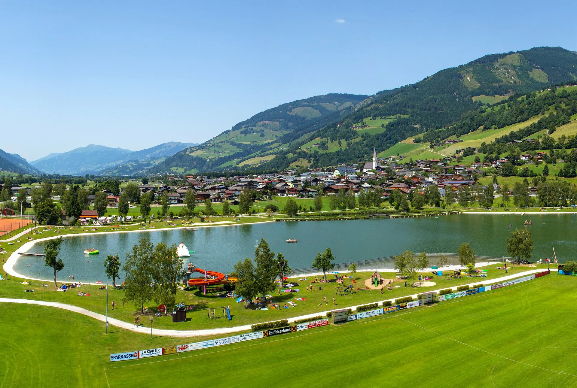 An idyllic lake nestled in a green landscape with views of gentle hills and mountains, complemented by well-maintained paths and a calm, inviting atmosphere.
