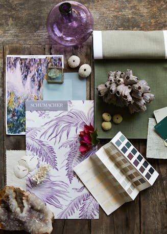 A wooden table with material and textile samples placed beside beach shells and a Pantone swatch pamphlet.