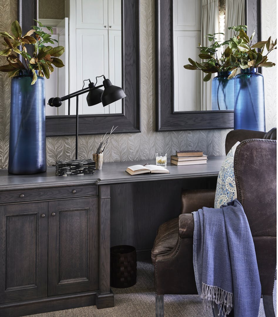 Two large blue vases and a modern table lamp are on top of an ebony-stained wood desk with two mirrors hung up on the wall.