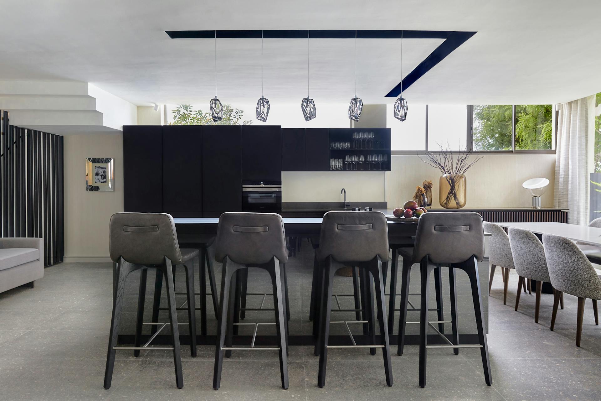 Four black barstools in the foreground with the kitchen in the background with a dining table and grey dining chairs to the right.