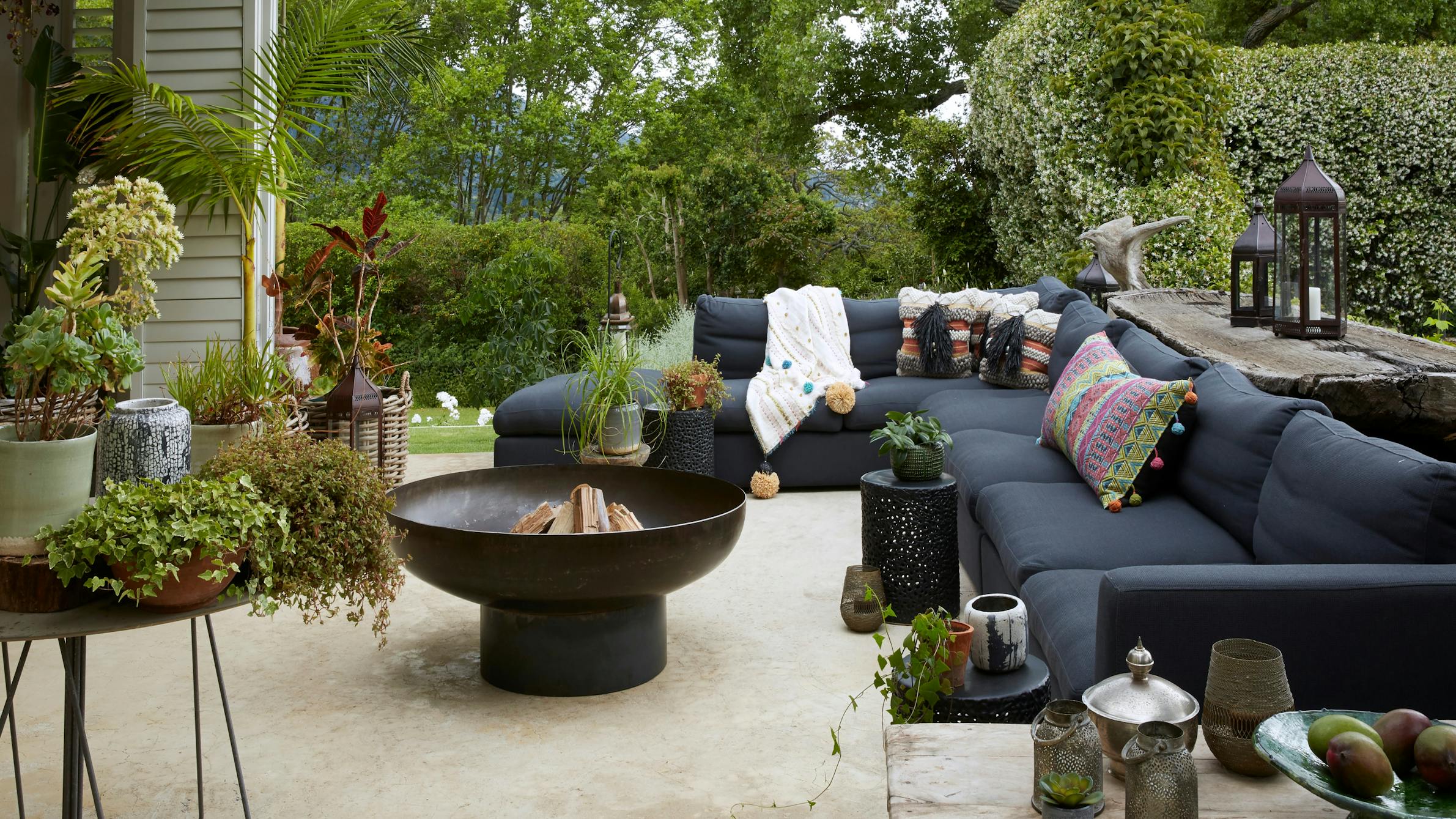 A Moroccan-inspired fire pit is surrounded by an outdoor sofa and lush greenery.