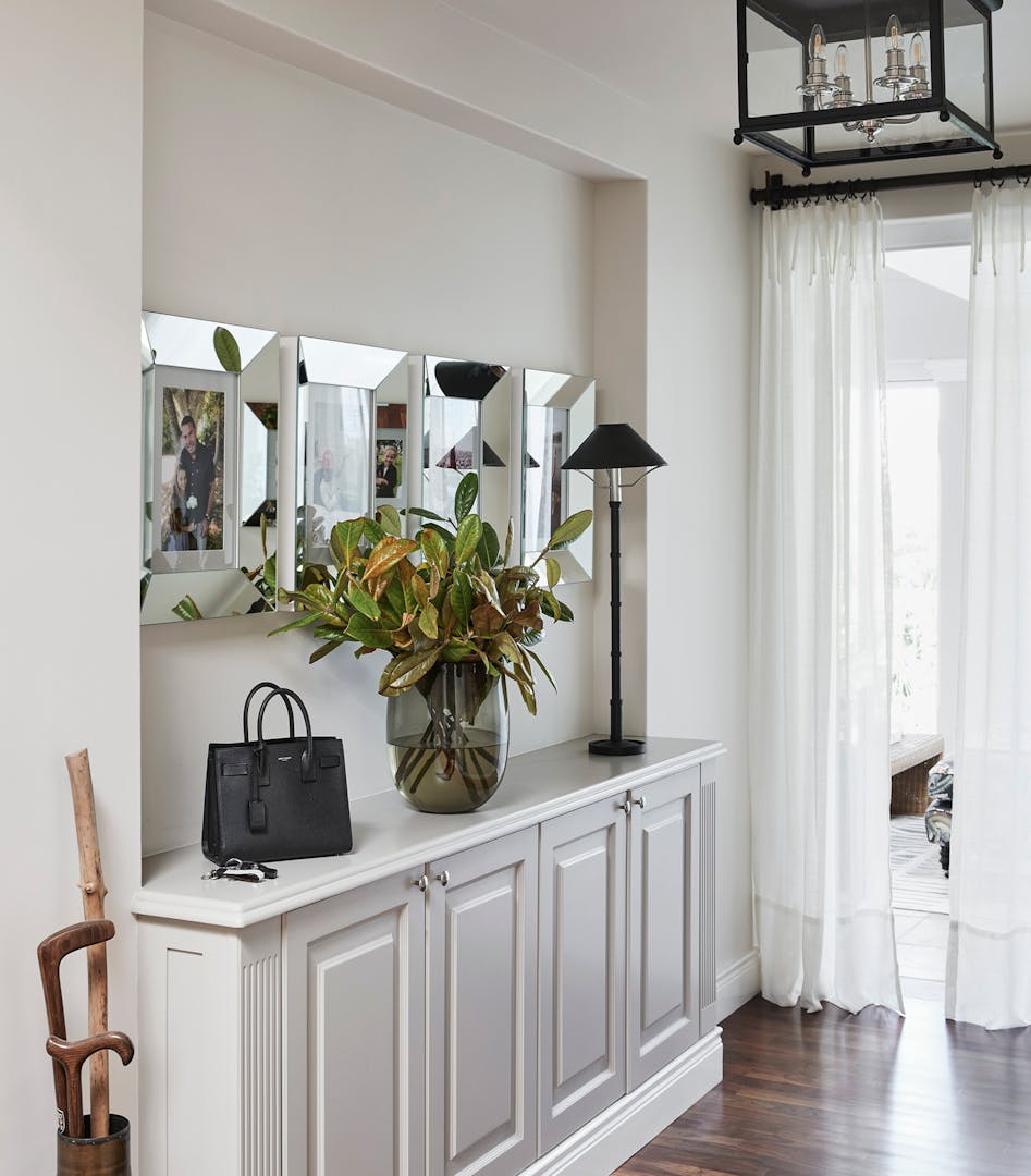 A console table with decorative accents including a vase, a bag and a lamp is placed below four picture frames.