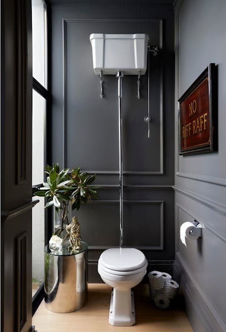A bathroom with a toilet in the middle, a steel side table to left and a framed artwork on the wall to the right.