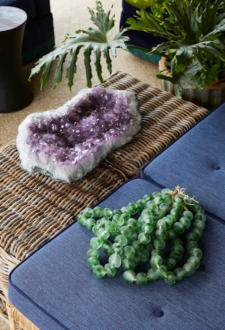 A purple crystal on top of a rattan side table and green beads on a blue cushion.
