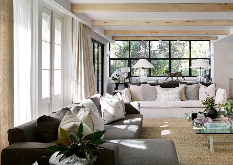 A contemporary living room with one grey, and one white sofa with large windows in the background.