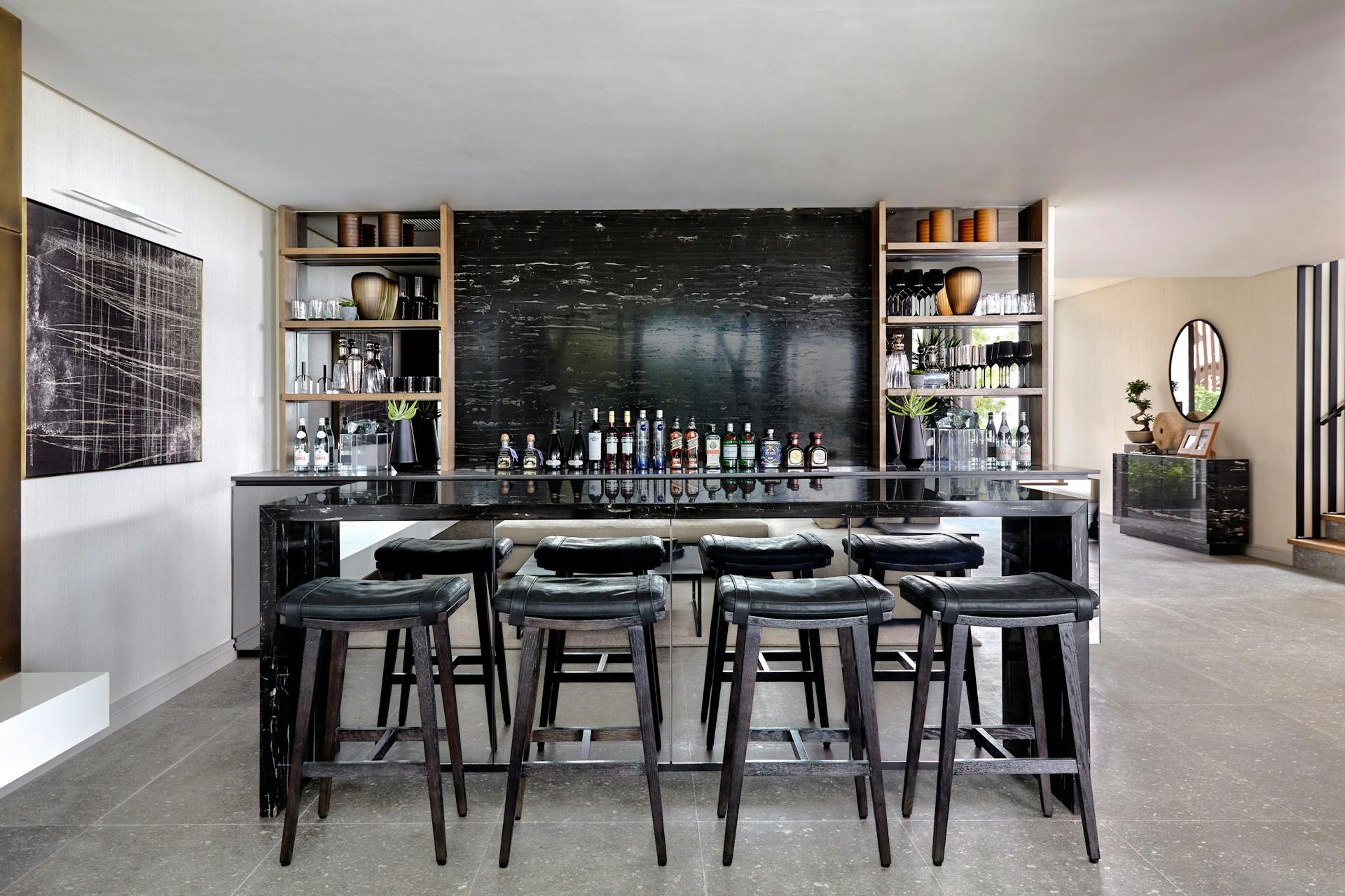 A bar area made out of black marble with 4 bar stools in the foreground and artwork to the left.