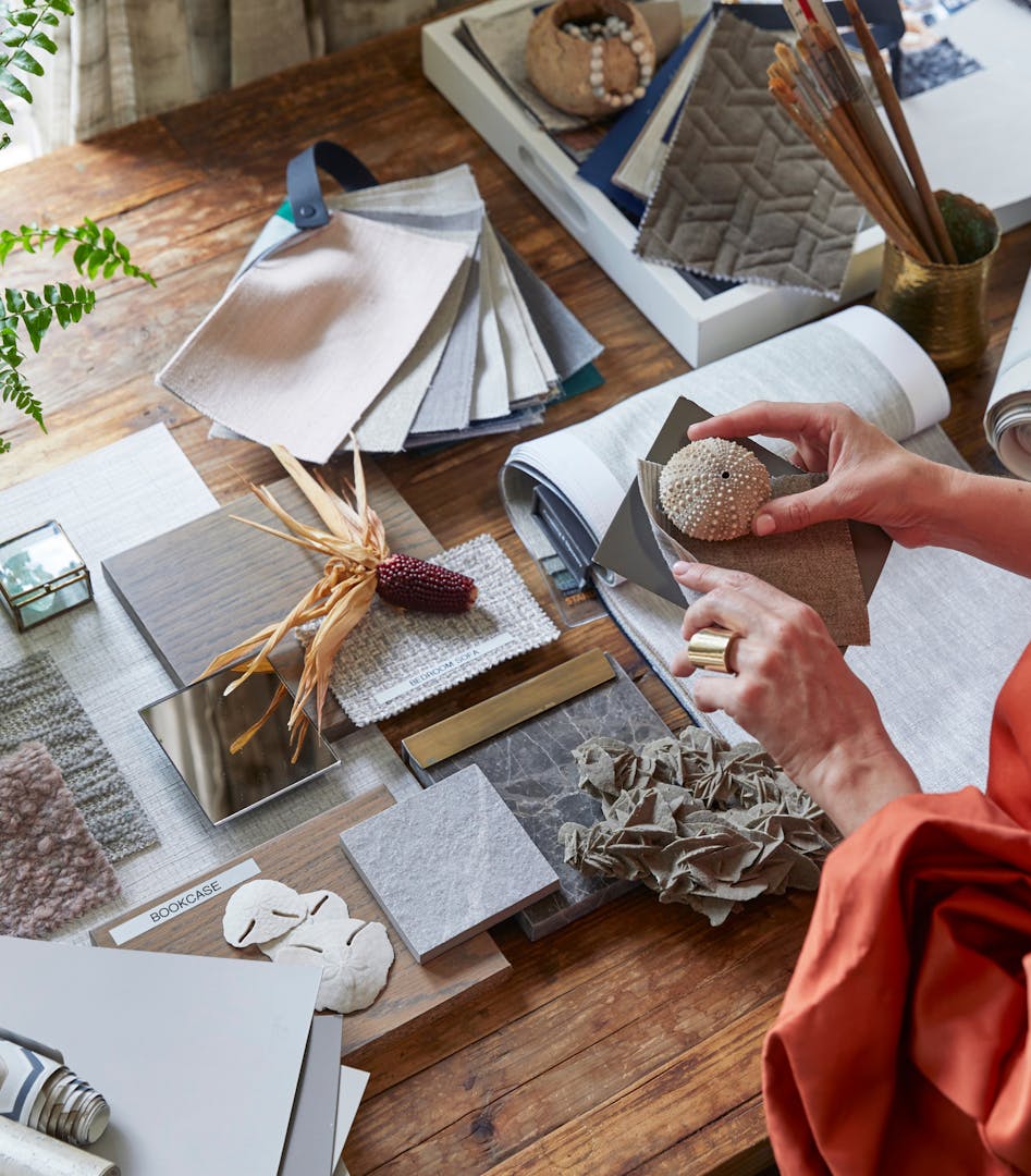 Simone Katherine's hands holding samples of fabric in the foreground with other samples of textures and fabrics on a wooden table in the background.