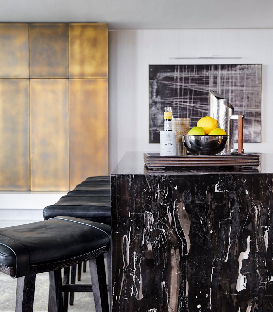 A waterfall, black marble bar with bar stools to the left and artwork with a similar pattern to the marble in the background.
