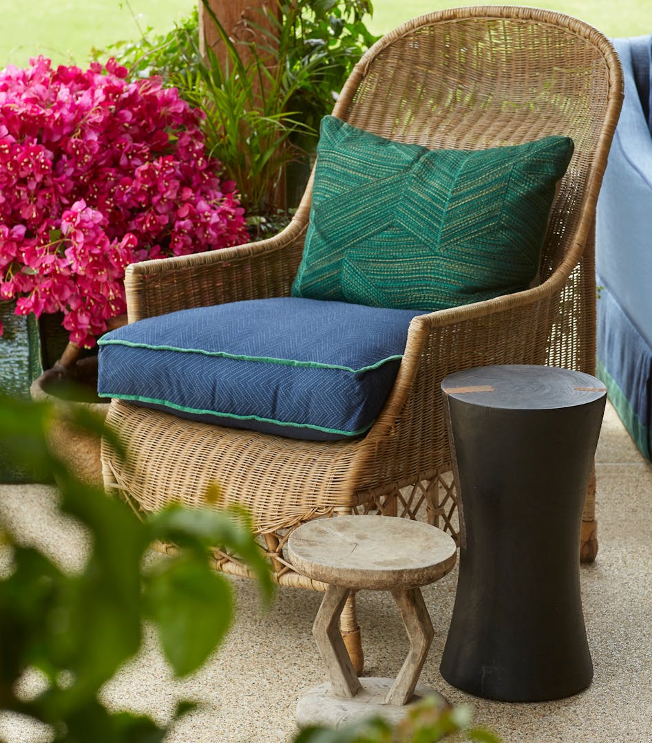 Two contemporary yet natural side tables in front of a rattan outdoor chair.