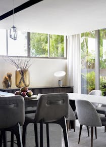 Modern, grey bar stools placed next to dining chairs, a dining table and a wooden console table with decorative accents in the background.