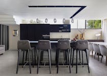 Four black barstools in the foreground with the kitchen in the background with a dining table and grey dining chairs to the right.