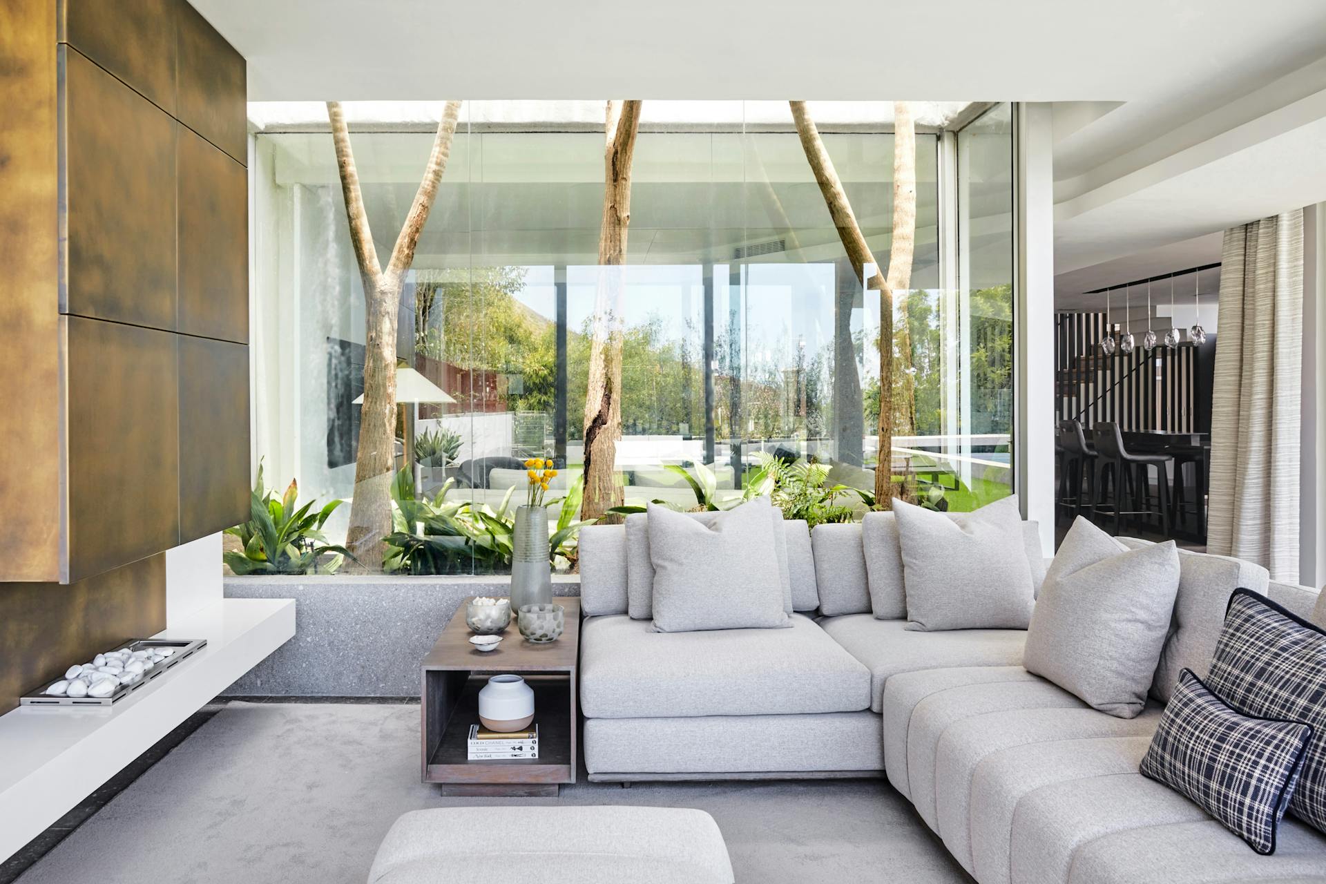 A modern living room with a grey sofa in the centre of the image and a wall clad in antique brass plates to the left.