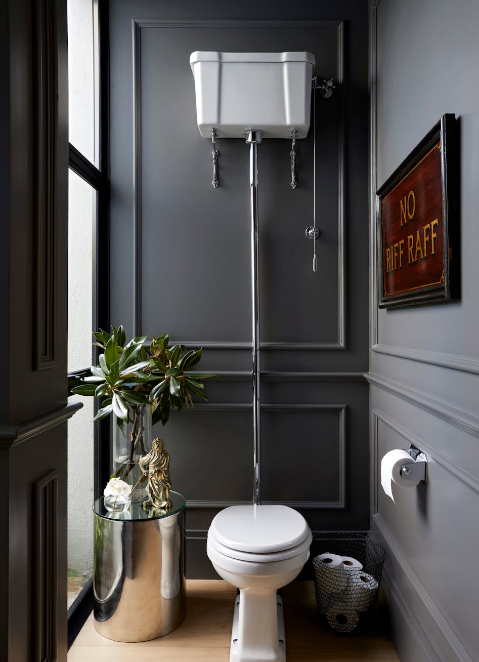 A bathroom with a toilet in the middle, a steel side table to left and a framed artwork on the wall to the right.