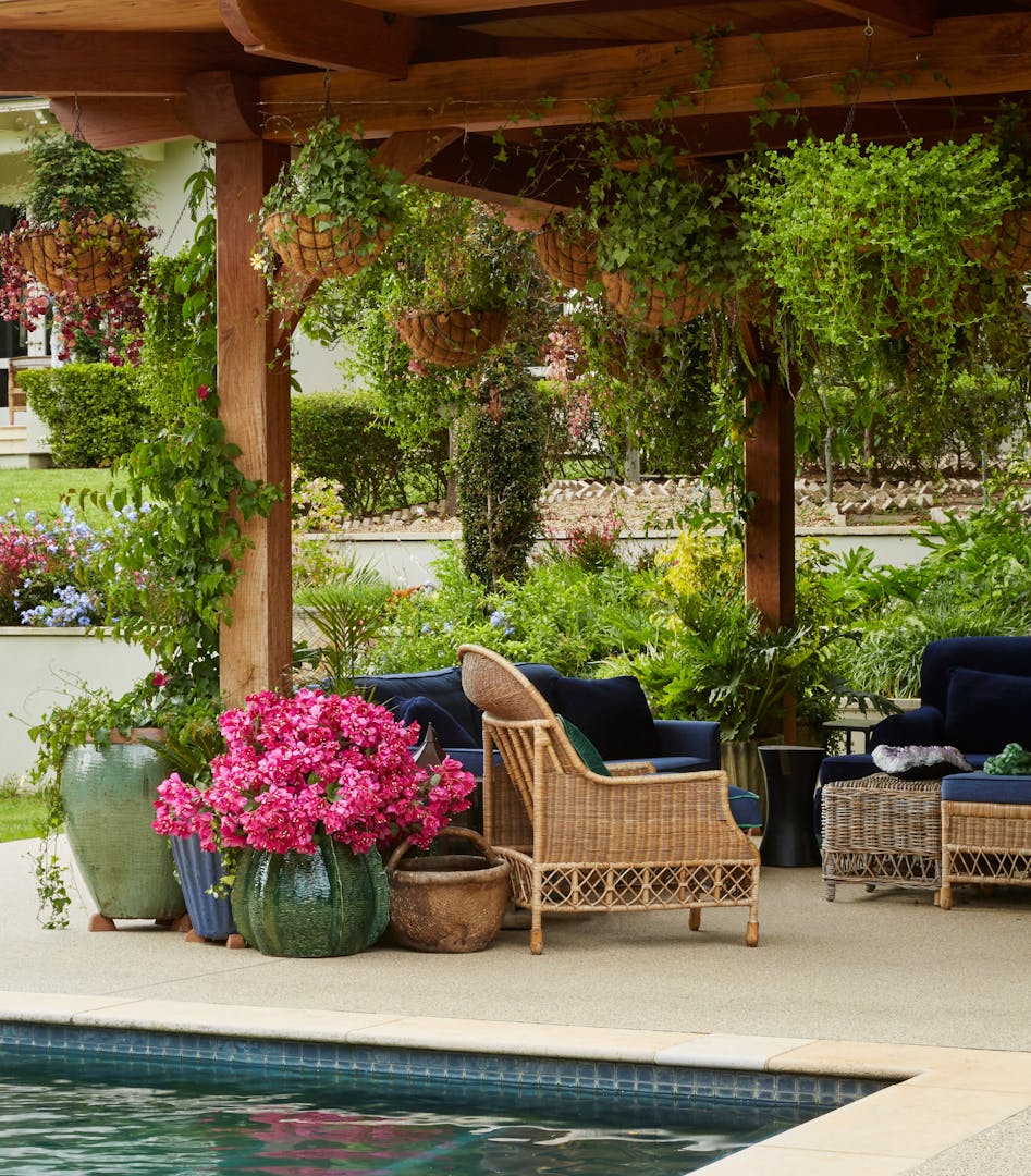 An outdoor entertainment area with rattan furniture with flowers in planters in the foreground.