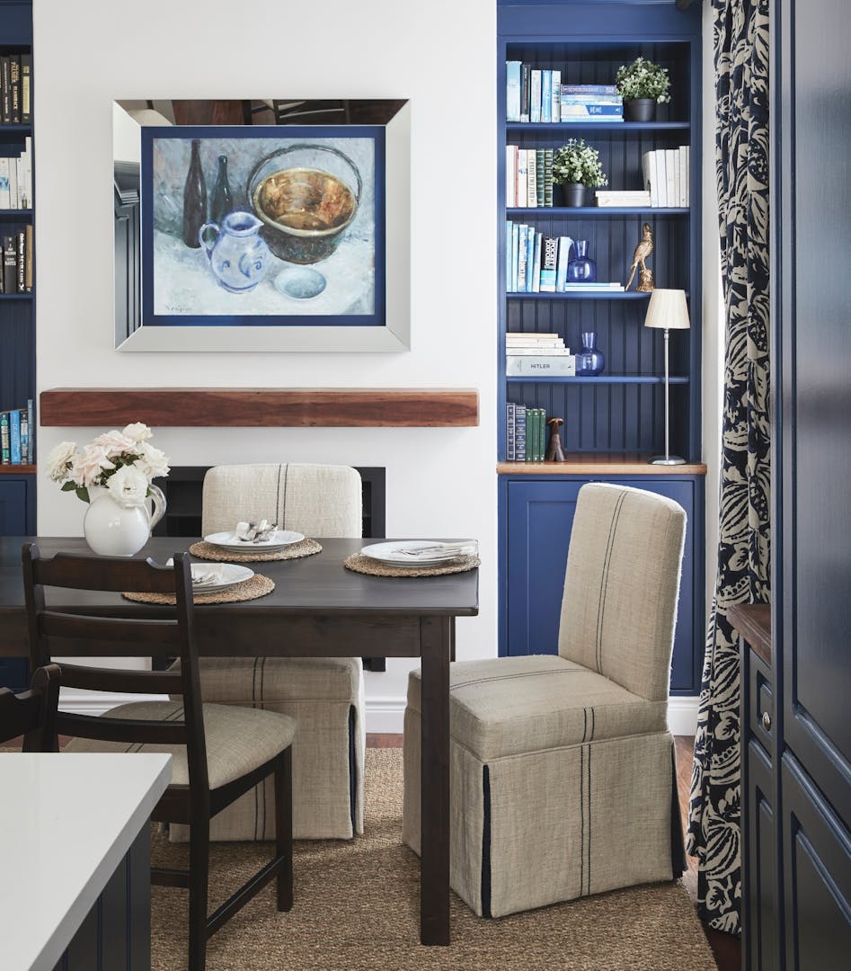 A dining area with a wooden dining table, fabric dining chairs and an artwork in blue tones on the wall.