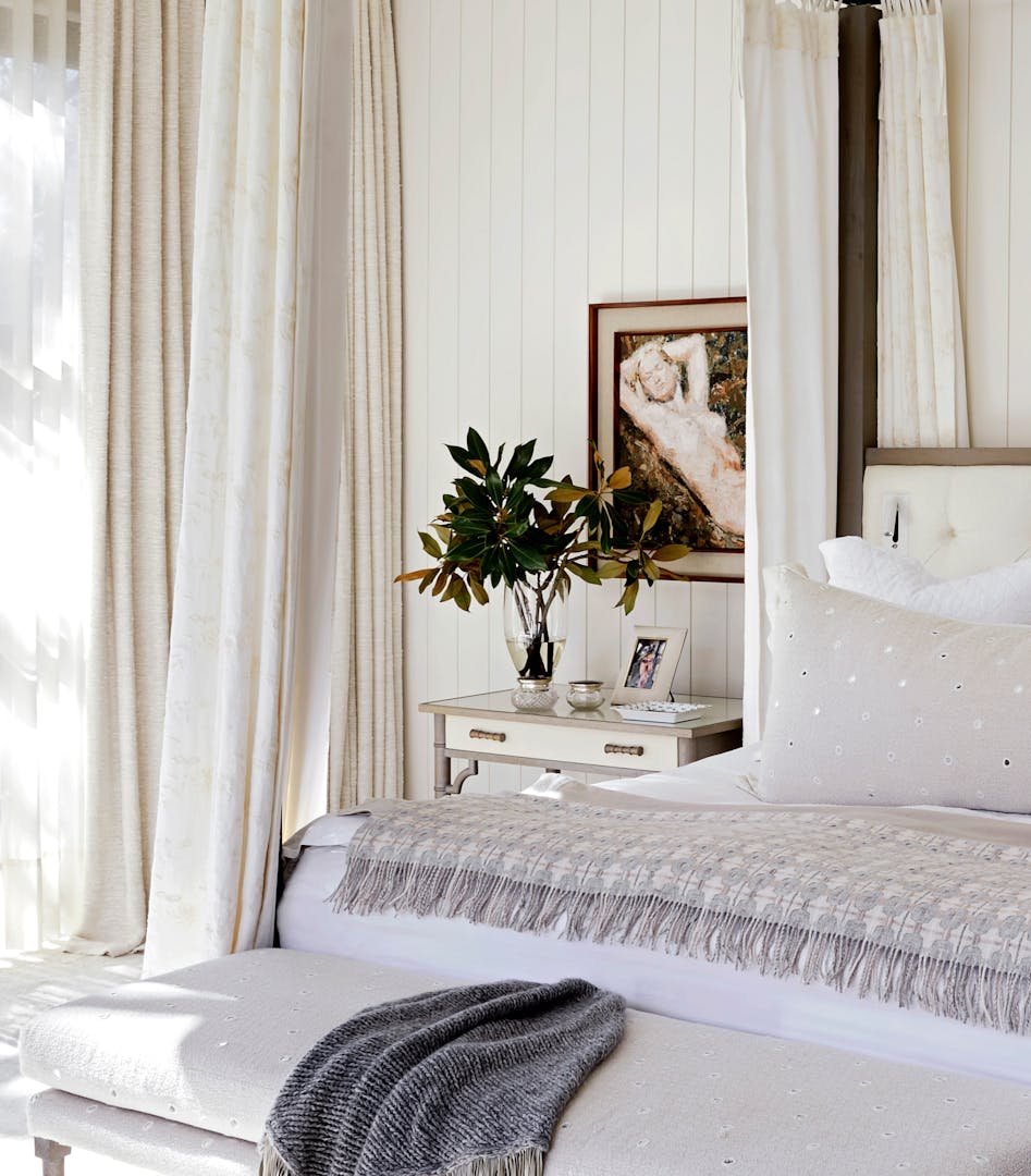 Close-up of a bedroom with a neutral colour palette. Artwork hangs just above a bedside that's placed next to a bed.