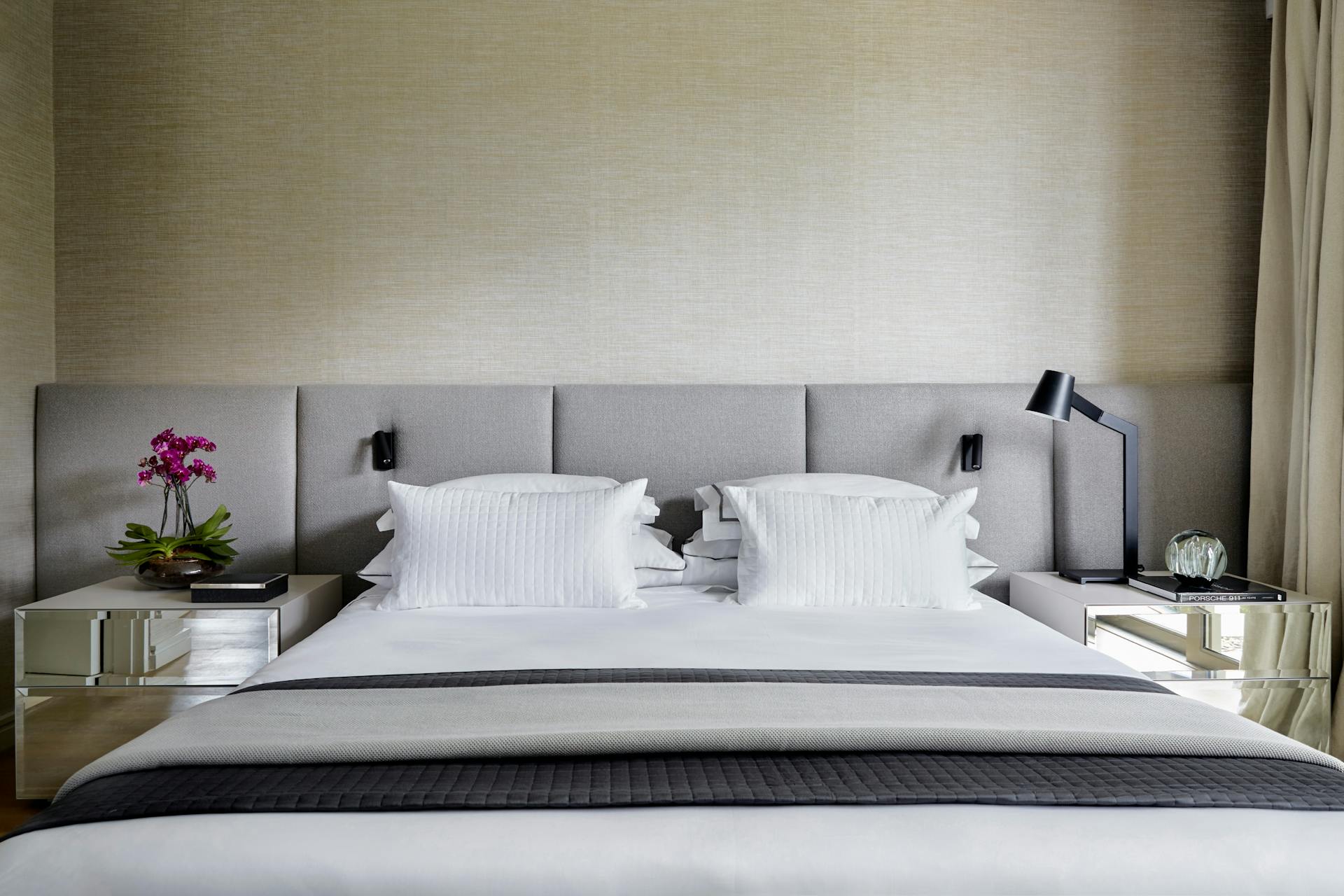 Close-up of a grey bed with a bedside table on either side. The bedding has a modern colour palette of whites, greys and black.