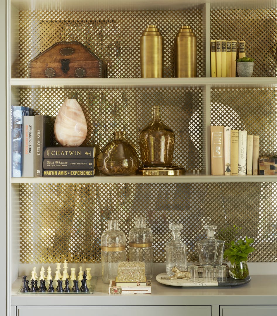 Three shelves hold books, vases and ornaments in various shades of cream, brown and gold, as well as a decanter and chess set.
