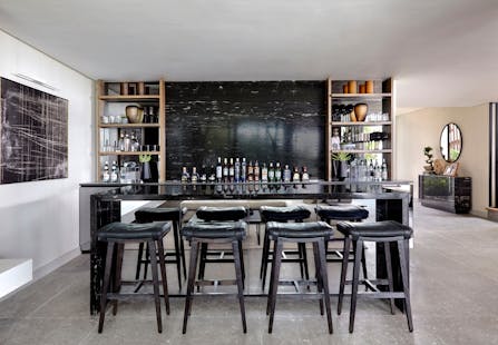 A bar area made out of black marble with 4 bar stools in the foreground and artwork to the left.