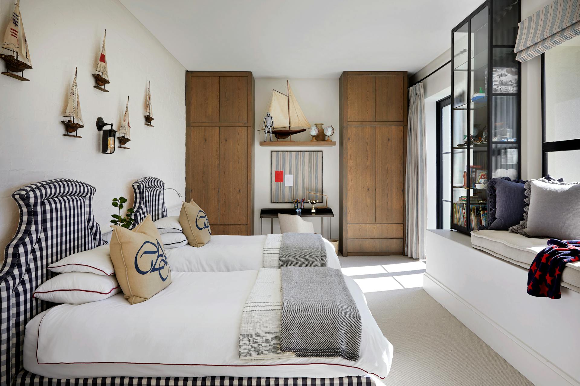 A nautical-themed bedroom with two single beds to the left, two wardrobes in the background and extra seating by the window to the right.