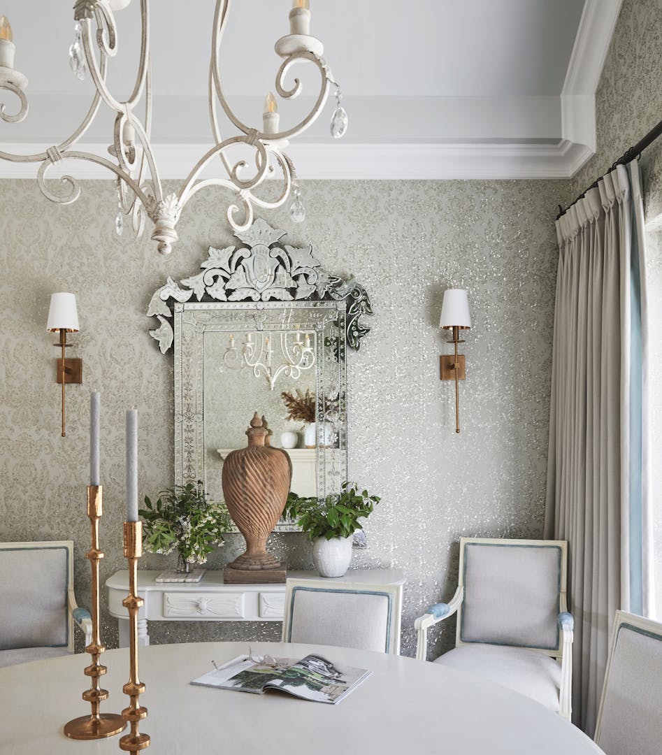 A French-style dining area with a chandelier at the top, a dining table with candelabras on top, with a mirror on the wall in the background.