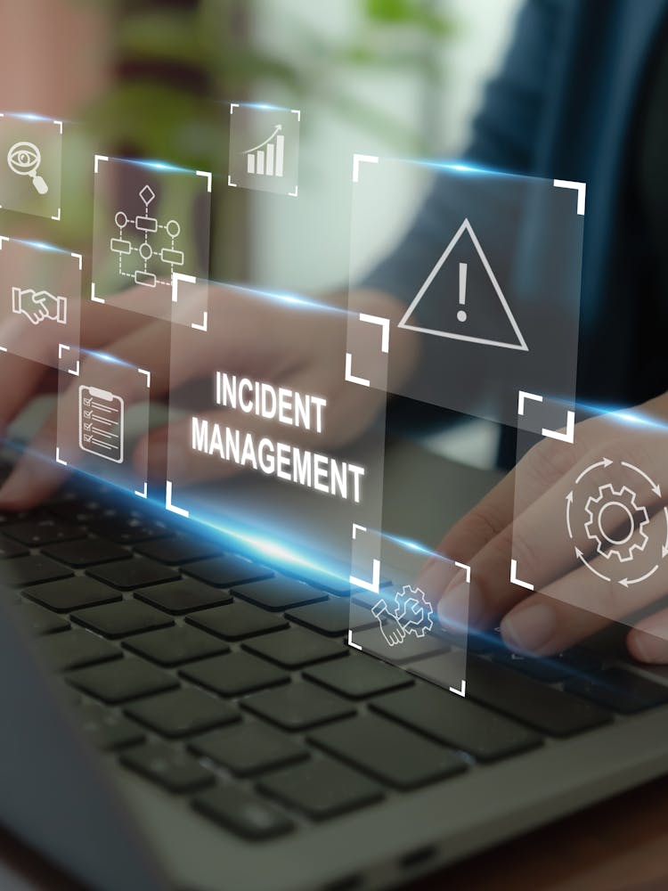 Person typing at a laptop displaying warning signs, evocative of cyber security. Error text reads Incident Management.