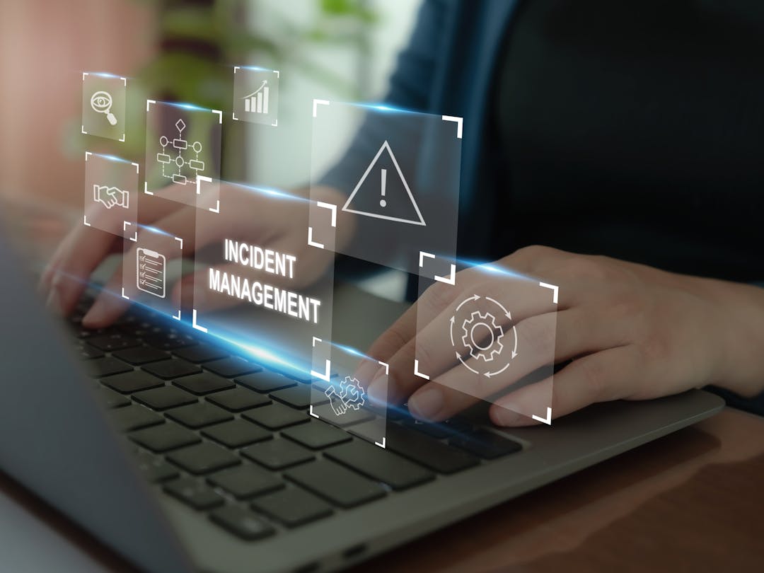 Person typing at a laptop displaying warning signs, evocative of cyber security. Error text reads Incident Management.