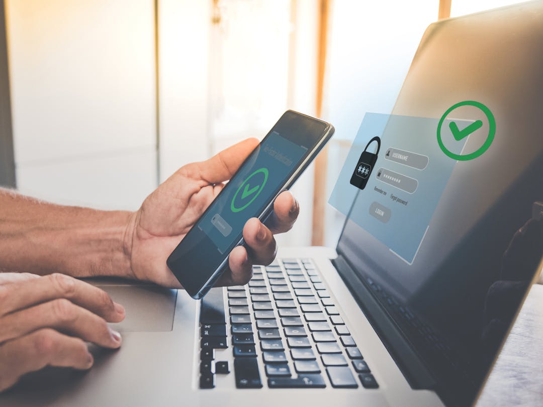 Person holding phone towards their laptop, with graphics representing authorisation, validation and security