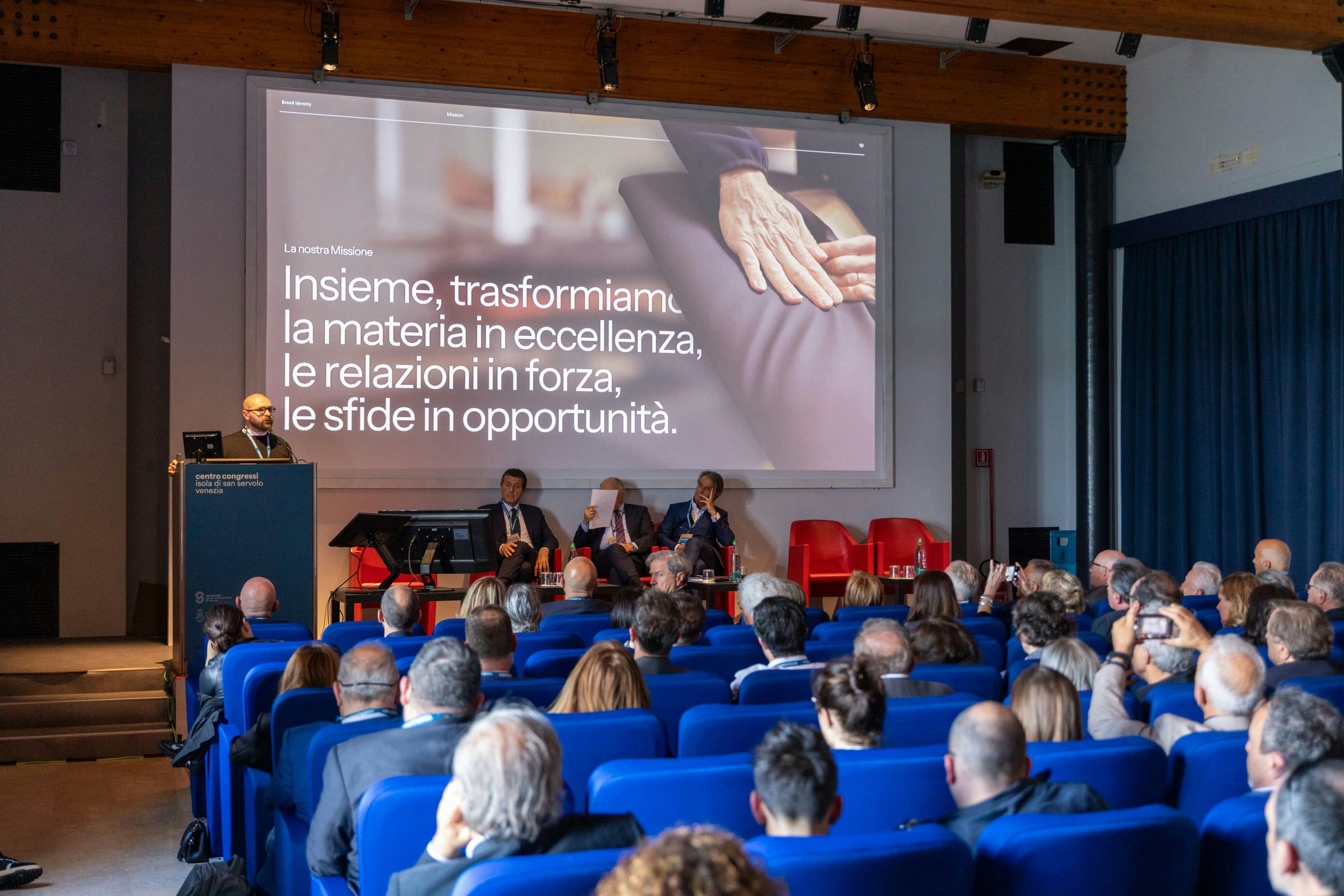 FederlegnoArredo business conference, with a speaker presenting the 'FLA as a future catalyst' strategy to an audience of wood-furniture sector professionals.