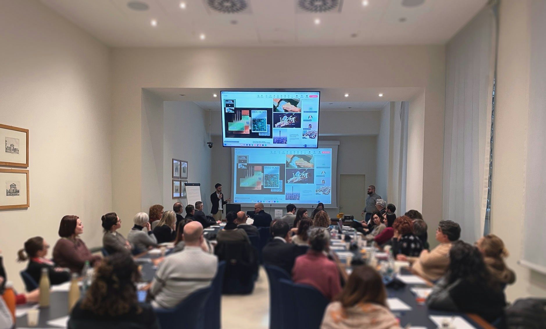 Collaborative workshop with wood-furniture stakeholders seated around a table, as presenters share projects on large screens. The image conveys active participation, co-creation of strategies, and innovation within the FederlegnoArredo ecosystem.