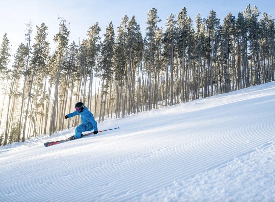 Skier skiing down a groomed run at Big Sky Montana resort as the sun gleams through the trees