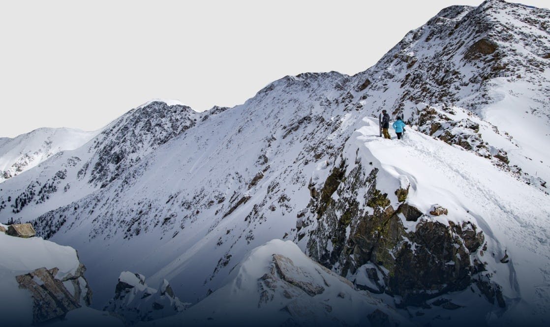 Two snowboarders hike up to the top of a snowy peak at Arapahoe Basin resort for alpine touring