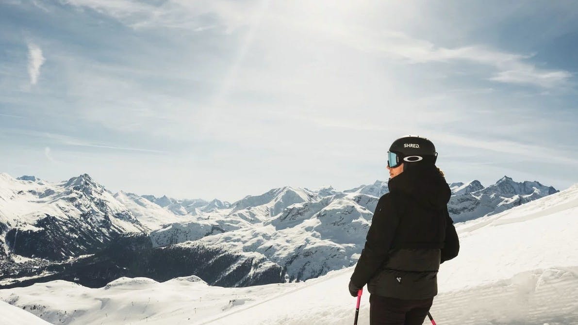 A skier wearing googles looks at the snowy mountains on a sunny day atop the slopes at St. Moritz resort