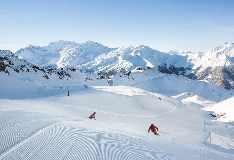 Two skiers enjoying freshly groomed slopes with a snowy mountain backdrop at Verbier Resort