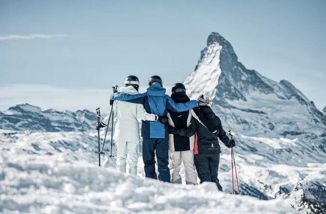 4 skiers with their arms around each other gaze at the snowy Matterhorn mountain from Zermatt Resort