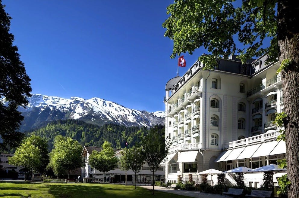 The building of Kempinski Palace Engelberg with a Switzerland flag and snowy mountains in the backdrop