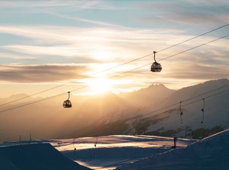 The gondola running during sunset at Crans-Montana ski resort with snowy mountains in the distance