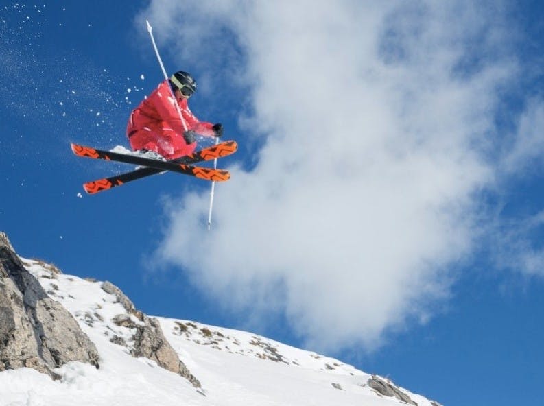 A skier does a cross trick in the air with a blue sky backdrop at Crans-Montana ski resort