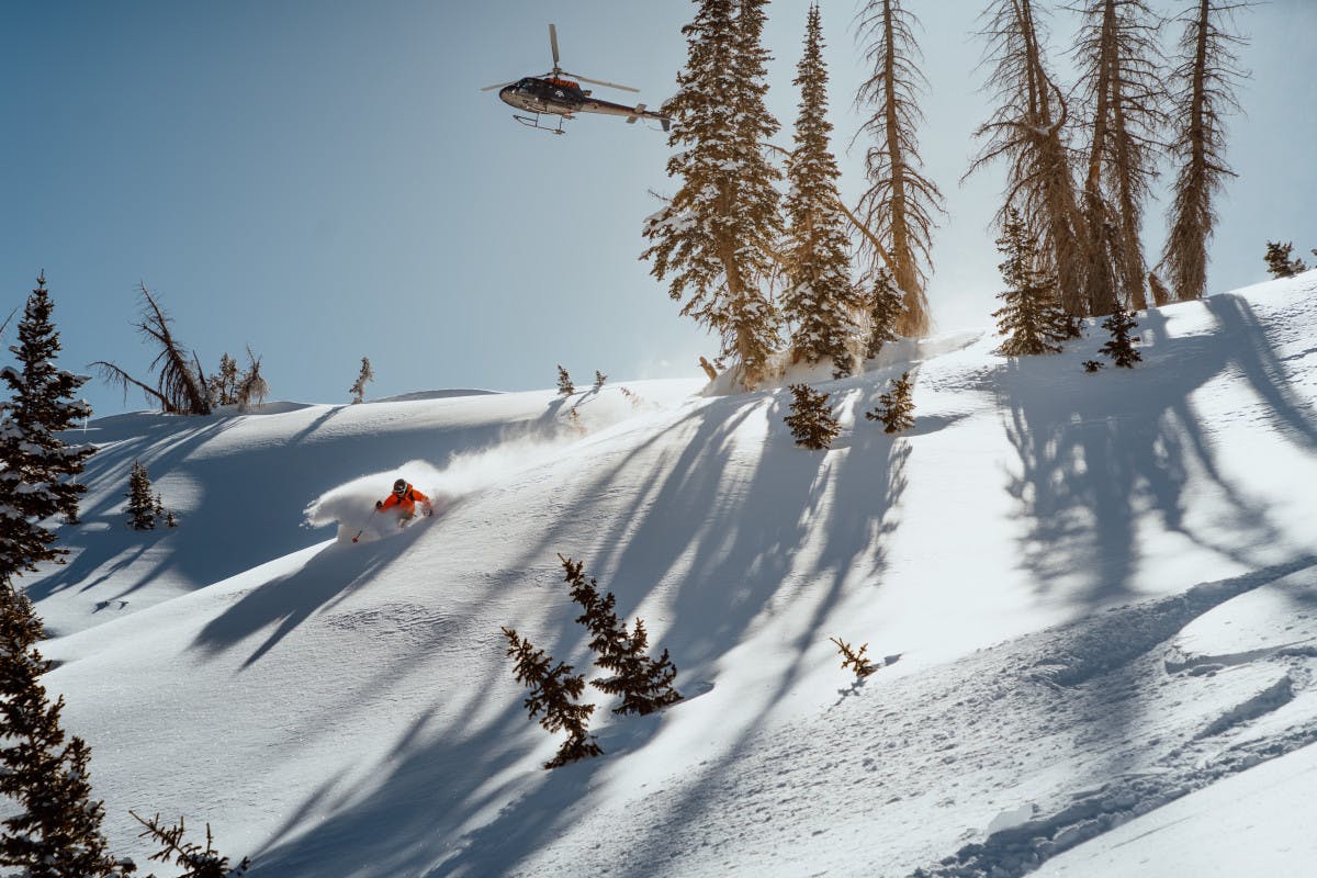 Skier in orange jacket hitting the slopes on a heli-skiing adventure in Utah thanks to Utah Powder Birds.