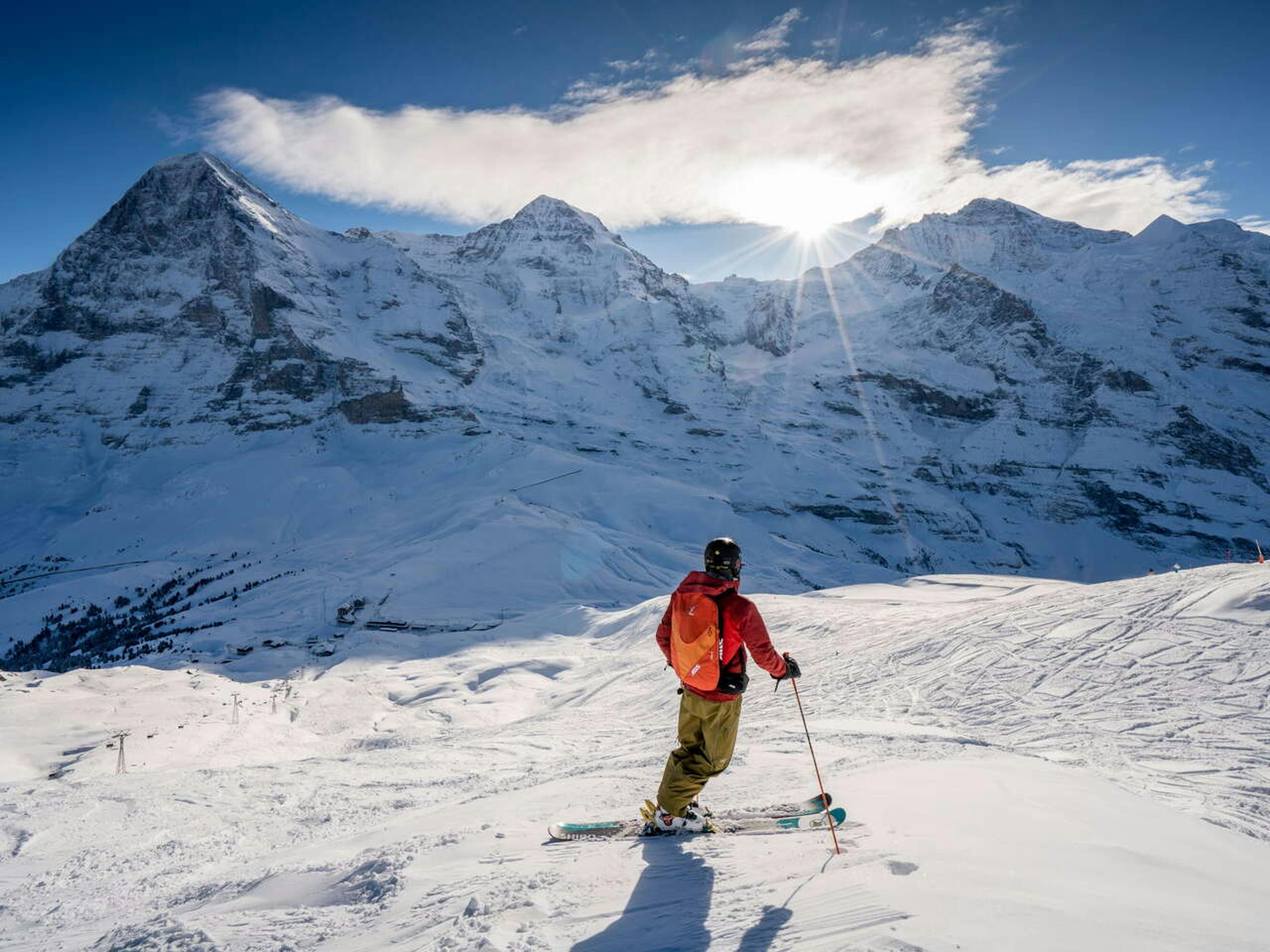 A male skier in orange ski jacket admiring the peaks at Grindelwald, Switzerland.