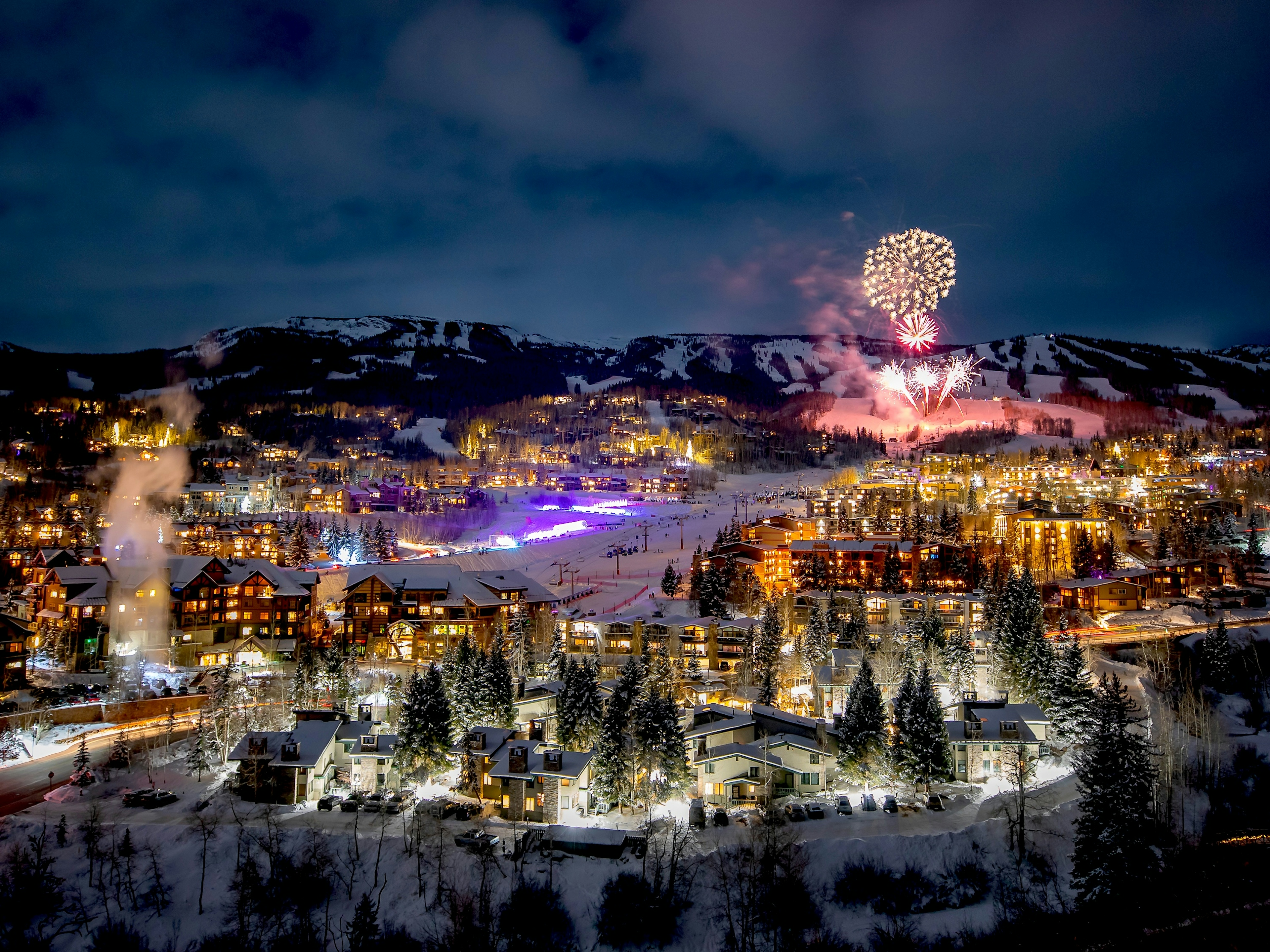 Colorful fireworks illuminate the night sky above a Colorado ski resort, creating a festive winter atmosphere.