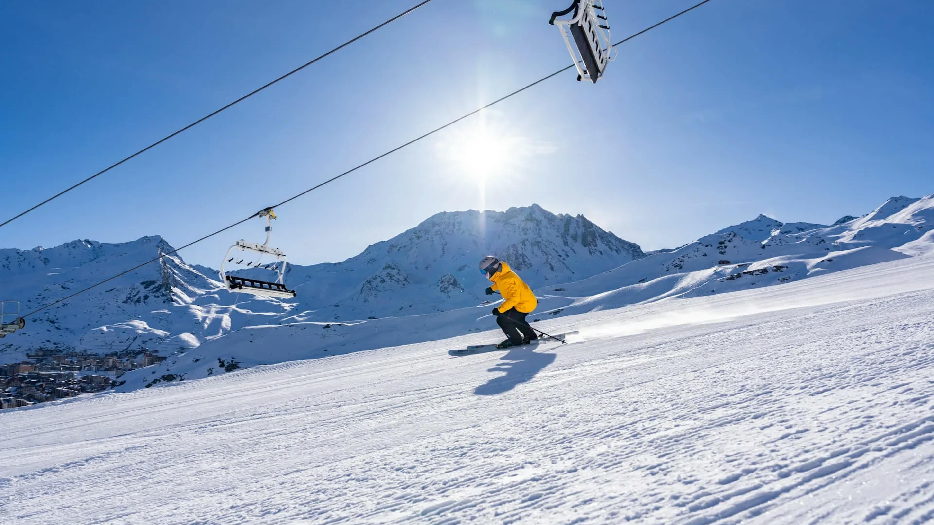 Skier of undiscernible gender in yellow ski jacket hitting the slopes at Val Thorens in France on a sunny day.