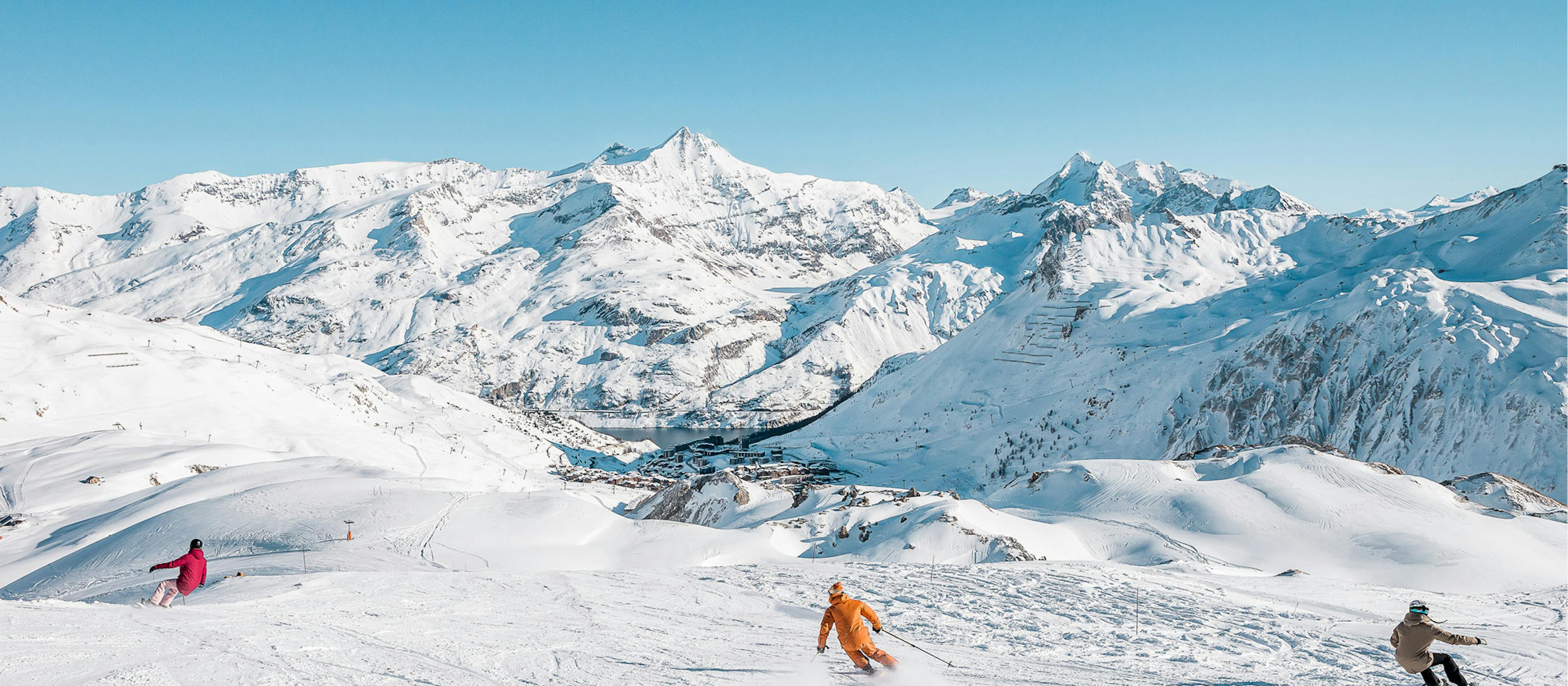 snowboarders and ski through tignes ski resort with mountains and the village in the background