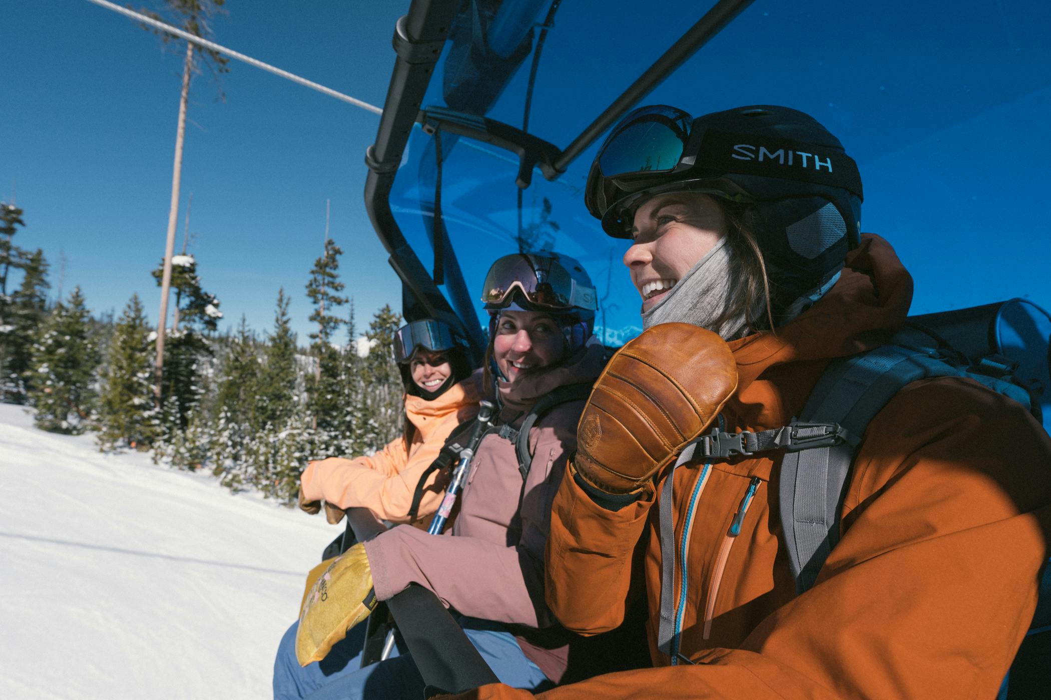 three people in ski gear smile and laugh on a ski lift at Big Sky Resort