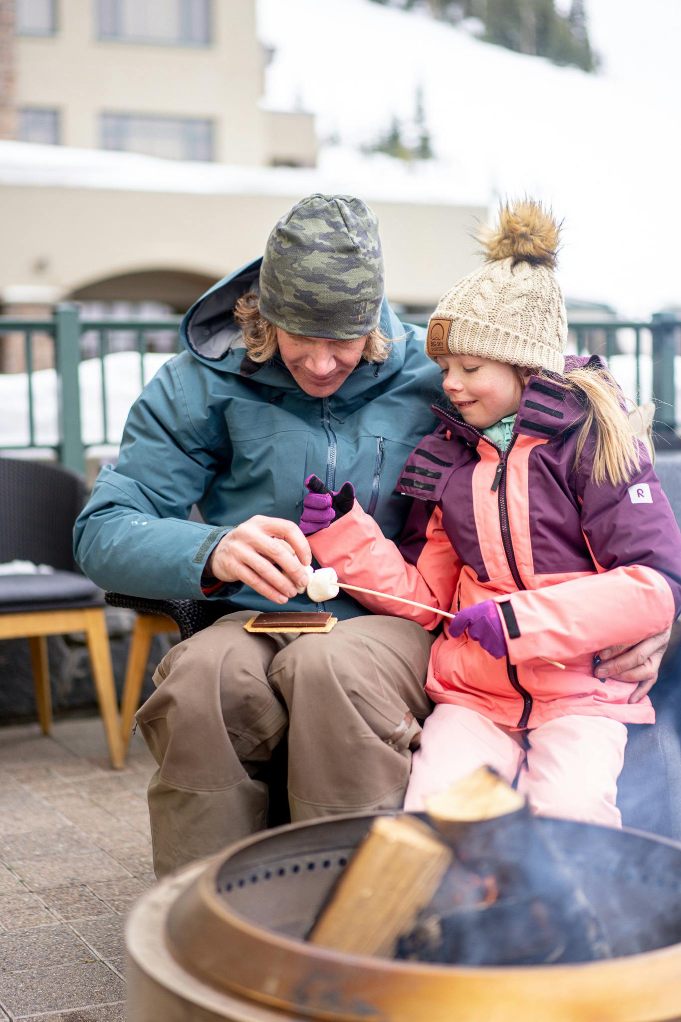 Dad and child put together s'mores sitting outside by a fire pit