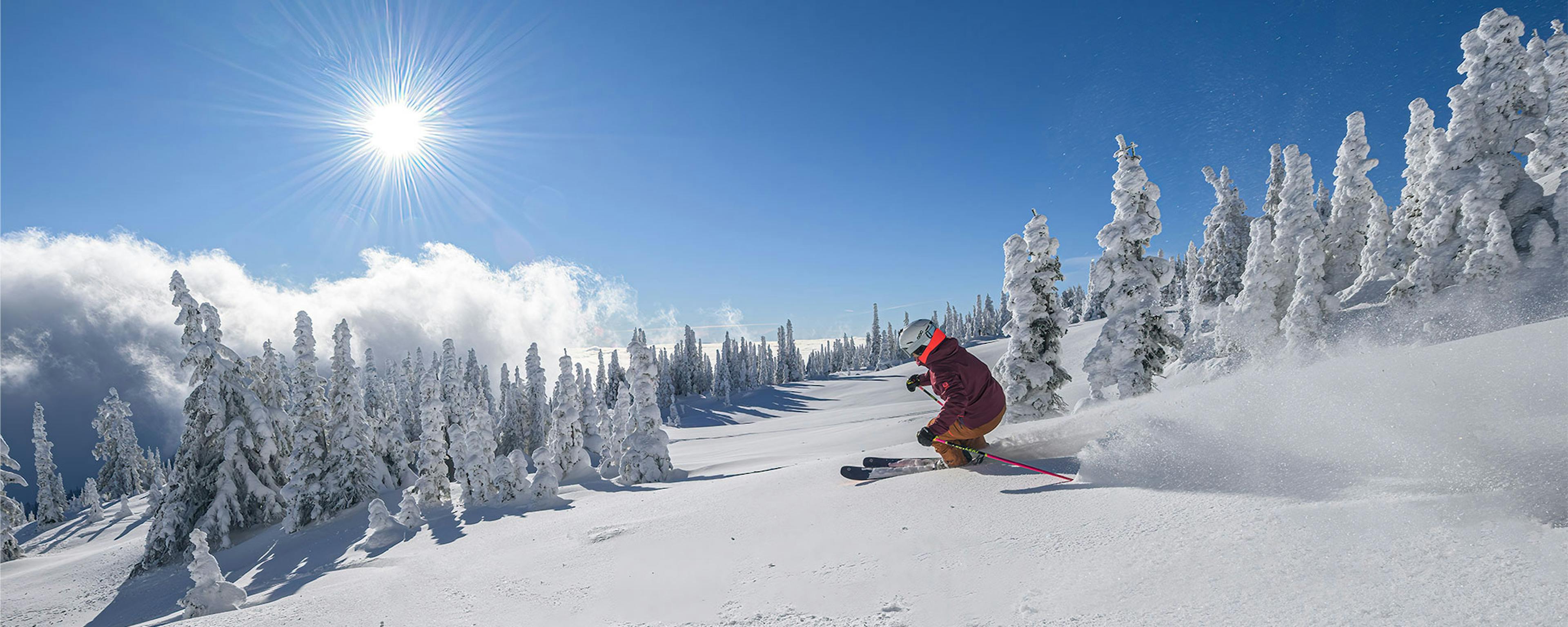 skier in a red jumpsuit on sunny snowy slopes at Big White Ski Resort BC